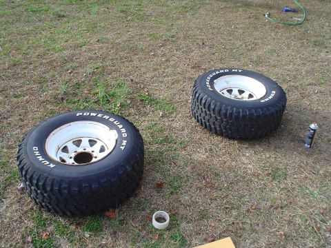1967 Ford F-250 - Two off-road tires with Kumho Powerguard MT branding sit on the grass next to a can of spray paint.