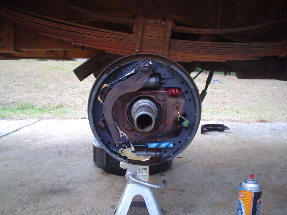 Vehicle brake drum assembly disassembled on jack stand. Leaf springs visible above