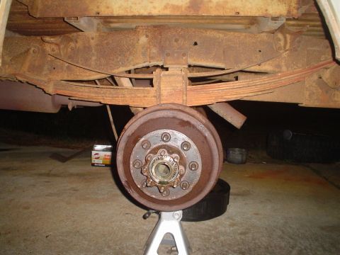 1967 Ford F-250 - The rear axle of a 1967 Ford F-250 is supported by a jack stand, revealing extensive rust on the drum brake and leaf springs.