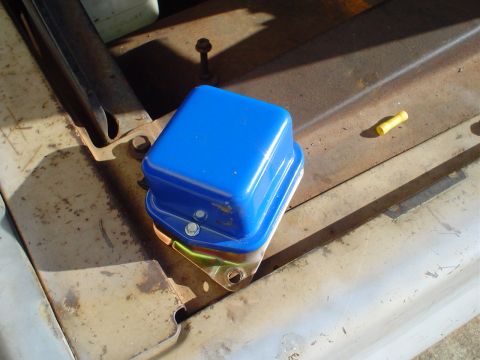 1967 Ford F-250 - Close-up of a blue voltage regulator, likely a replacement part, on a weathered metal surface.