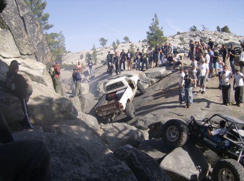 1986 Ford Bronco - Off-roading event with multiple vehicles and onlookers on a challenging rocky course.