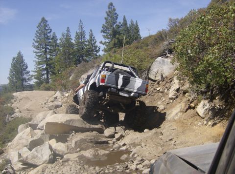 1986 Ford Bronco - A modified off-road vehicle navigates a challenging rocky terrain on a sunny day.