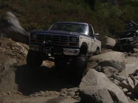 1986 Ford Bronco - Modified pickup truck tackles a challenging rocky off-road course, with another vehicle visible in the background.
