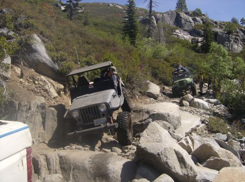 1986 Ford Bronco - Two Jeeps tackle a challenging rocky off-road trail under a clear blue sky.