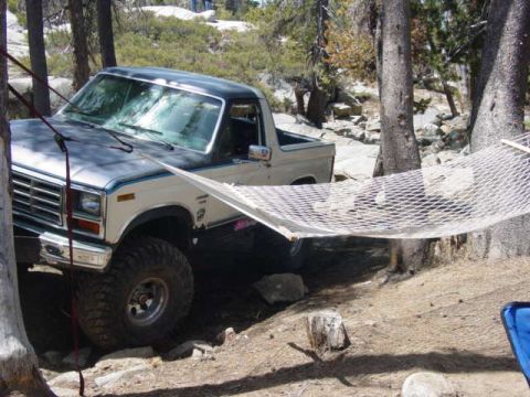 1986 Ford Bronco - A 1986 Ford Bronco is parked in a wooded area, with a hammock strung between trees in the foreground.
