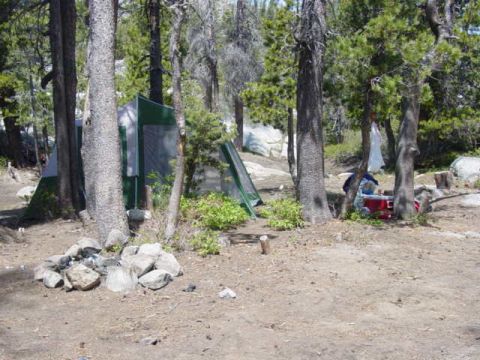 1986 Ford Bronco - A campsite scene with tents set up among trees, a rock fire pit, and camping gear visible.