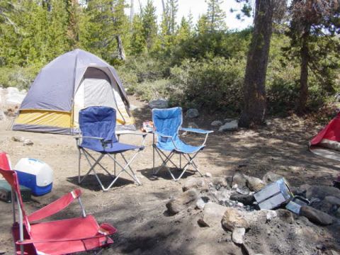 1986 Ford Bronco - A campsite is set up with tents, chairs, and a fire pit in a wooded area.
