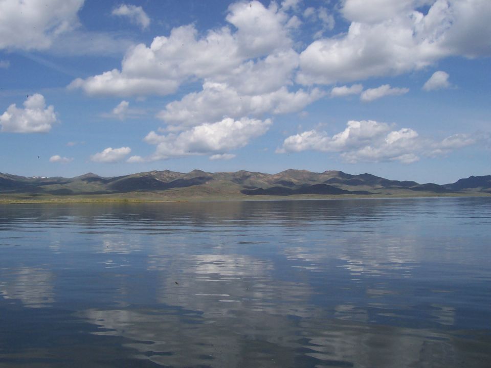 Lake with reflections of clouds and mountains under a blue sky with white clouds
