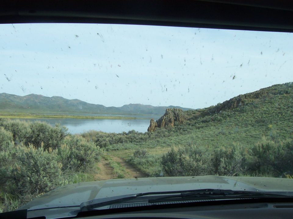 Interior view of a dusty windshield looking out at a lake and hills