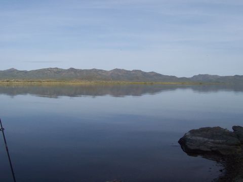 1994 Ford F-150 - A calm lake reflects mountains under a clear sky, with a fishing rod visible.