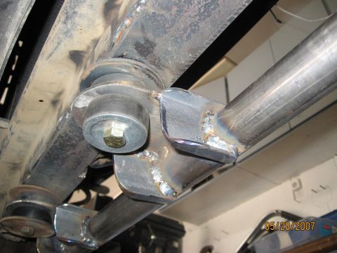 1994 Ford Bronco - Welded metal suspension components with visible bolts and rubber bushings, taken from underneath a vehicle.