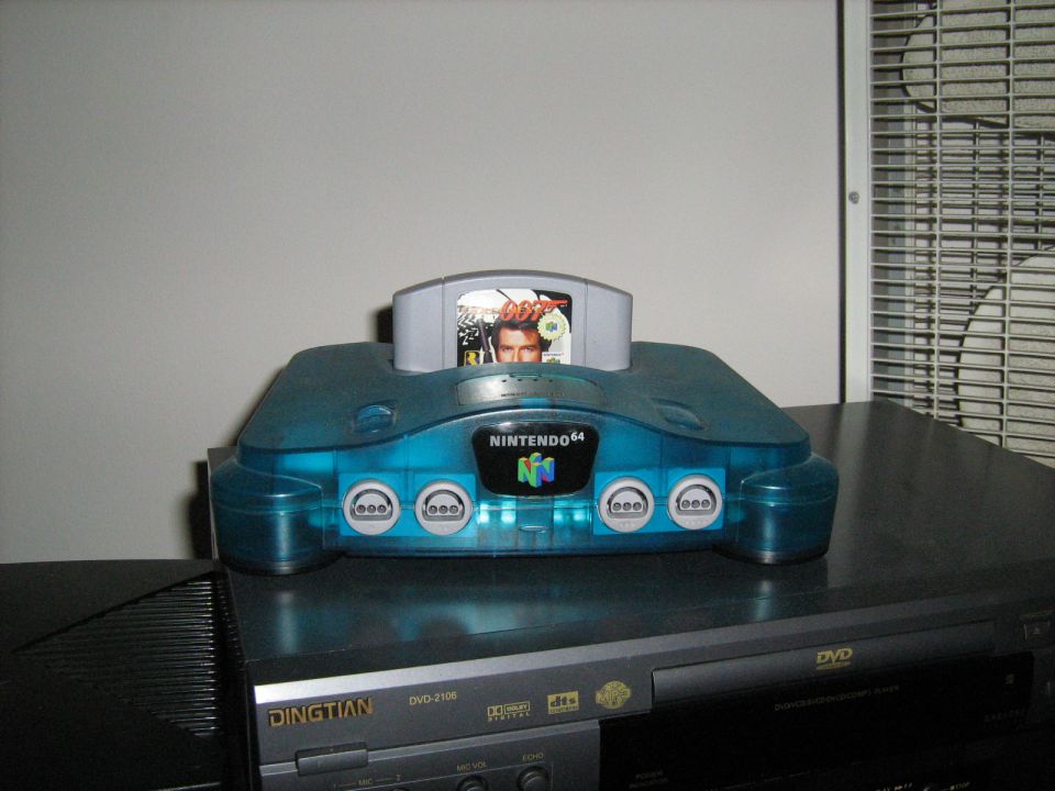 Translucent blue Nintendo 64 console with a game cartridge sitting on a DVD player