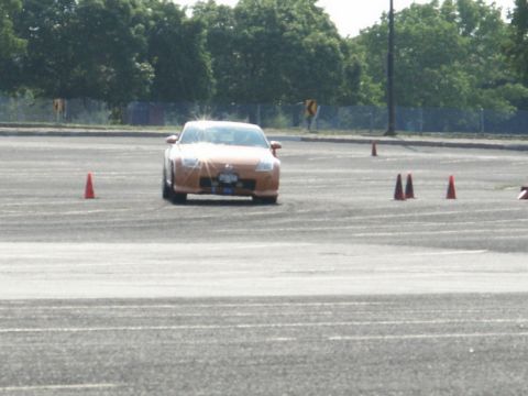 2001 Mercury Grand Marquis - An orange sports car drives through a course marked by traffic cones on a paved lot.