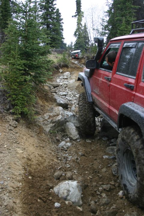 2003 Jeep TJ - A red 2003 Jeep Cherokee XJ navigates a challenging rocky trail, with another Jeep visible further up the path.