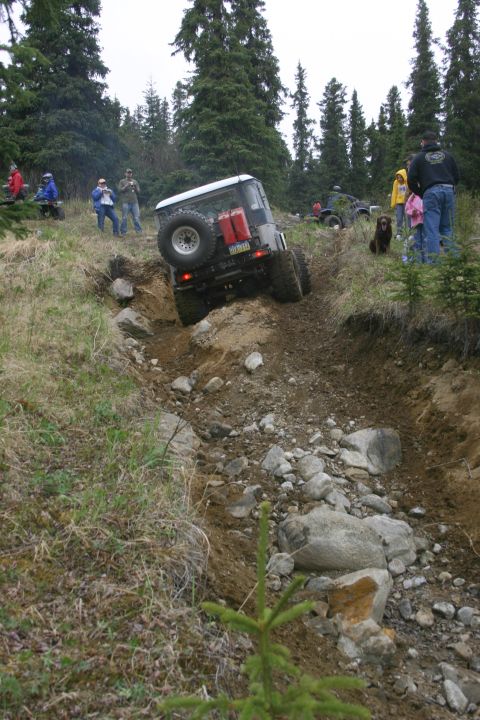 2003 Jeep TJ - An off-road vehicle navigates a challenging, rocky terrain with spectators observing the action.
