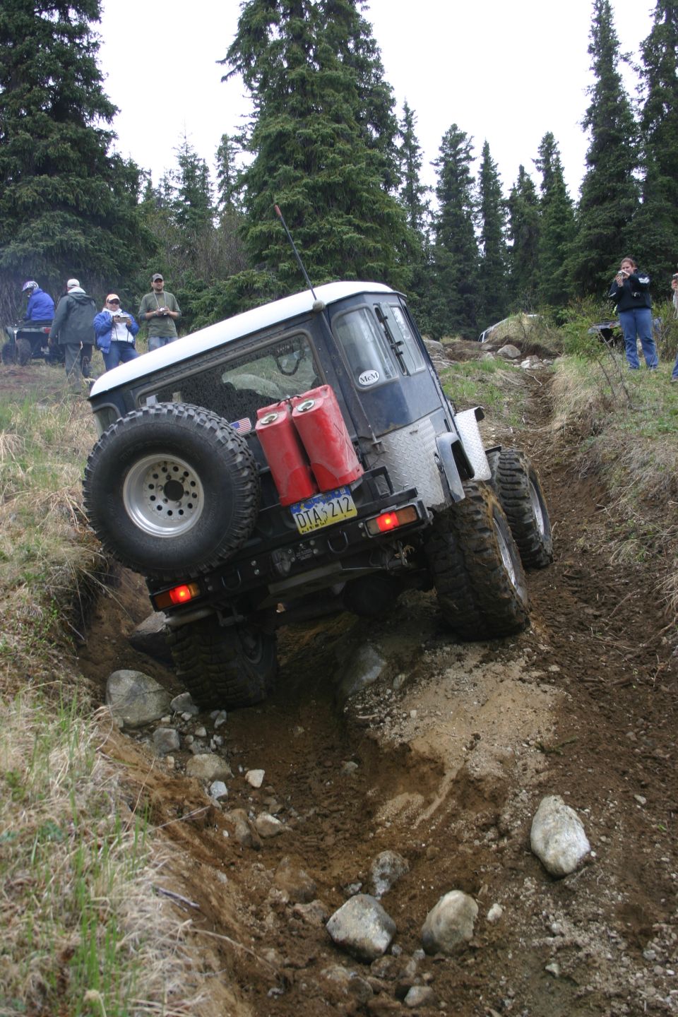 Off-road vehicle with spare tire and gas cans navigating a muddy trail