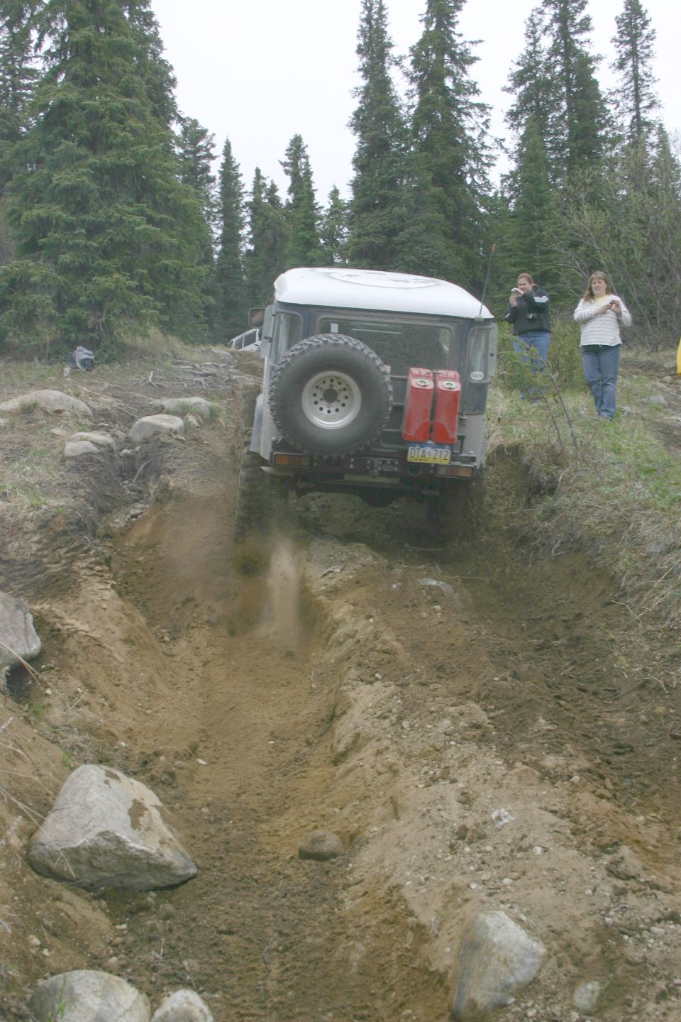 Toyota Land Cruiser FJ40 driving through a rutted dirt track, with two red jerry cans mounted on the rear door