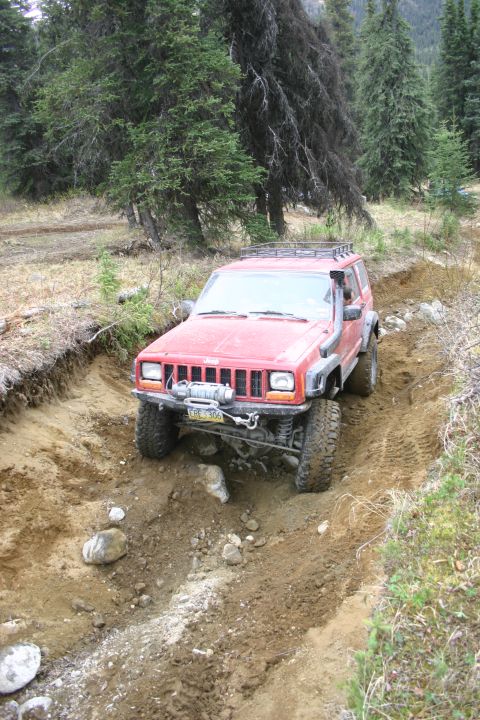 2003 Jeep TJ - A red Jeep Cherokee XJ navigates a challenging dirt path, equipped with a snorkel for off-road adventures.