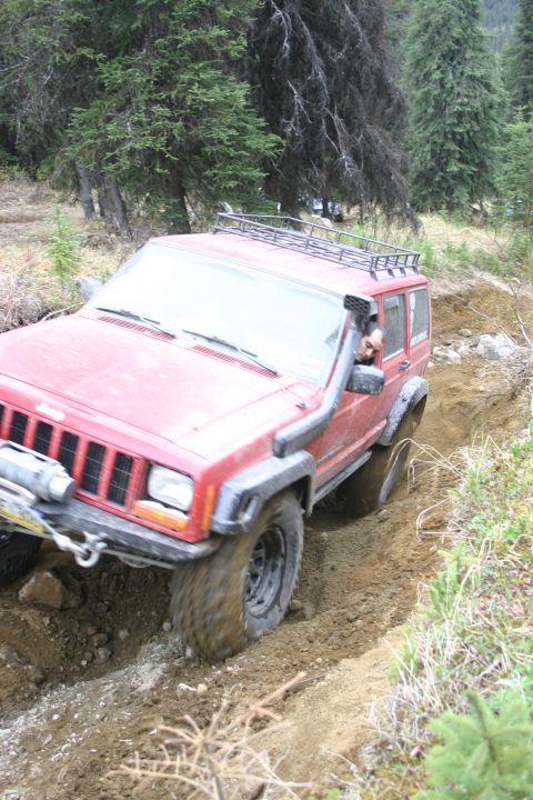 2003 Jeep TJ - A red 2003 Jeep Cherokee XJ tackles a challenging off-road trail, demonstrating its capability on rough terrain.