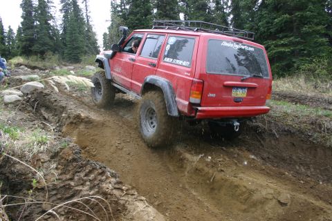 2003 Jeep TJ - A red Jeep Cherokee XJ navigates a challenging dirt trail with a snorkel and roof rack.