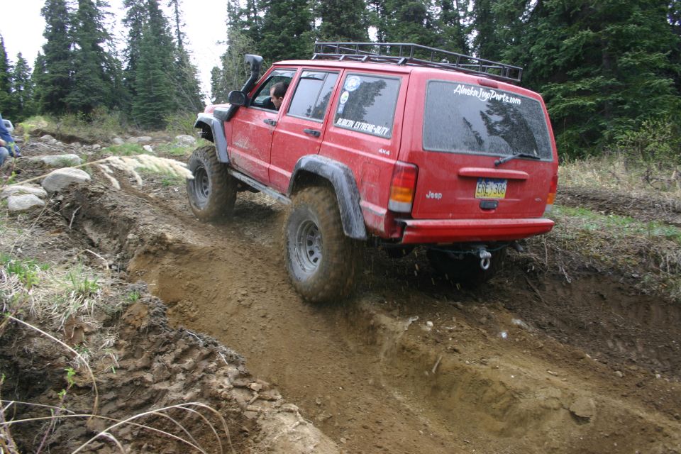 Red Jeep Cherokee XJ off-roading on a dirt track, rear view, with snorkel and roof rack