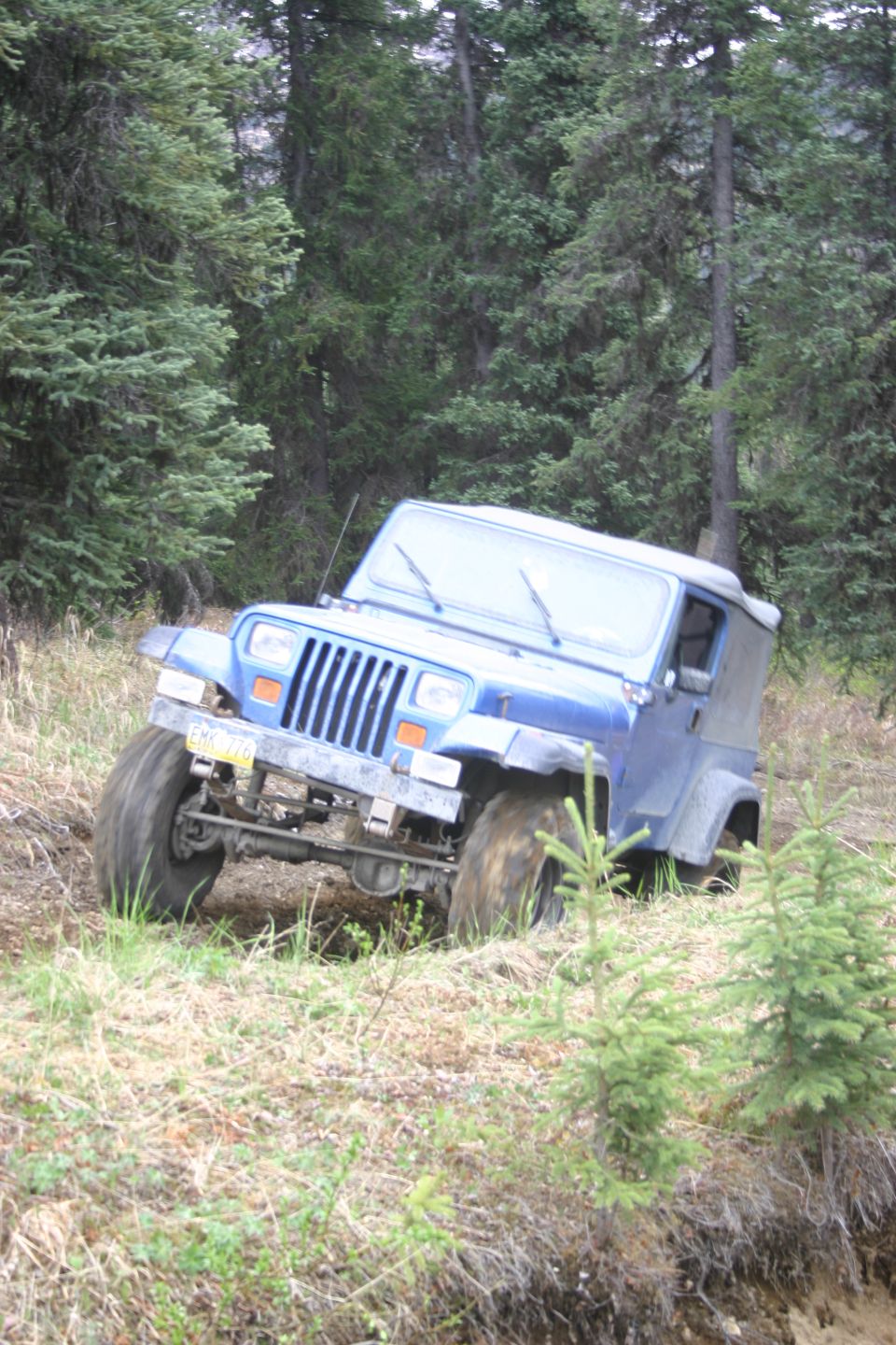 Blue Jeep Wrangler with soft top driving off-road, tires kicking up dirt