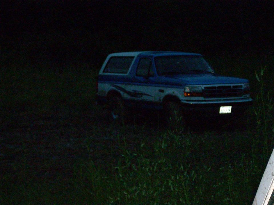 Blue and white Ford Bronco parked in a grassy field at night, passenger-side front view