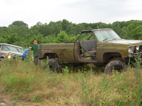 1992 Ford Bronco - An olive green pickup truck with a roll cage and off-road tires is parked in a grassy field next to another vehicle.