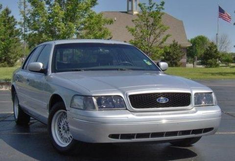 2002 Ford Crown Victoria - Silver 2002 Ford Crown Victoria parked outdoors with a building and flag in the background.
