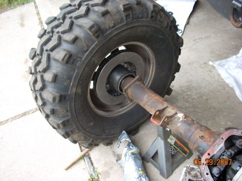 2000 Chevrolet Tahoe - Close-up of a rusty axle assembly and a large tire, supported by a jack stand.