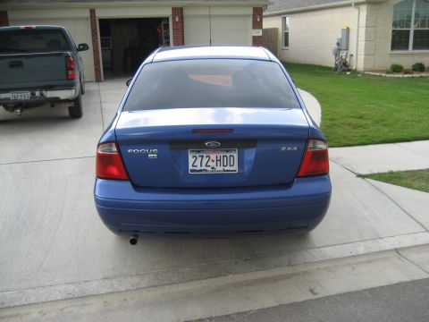 1986 Ford Bronco - Rear view of a blue Ford Focus sedan parked in a driveway next to a pickup truck.