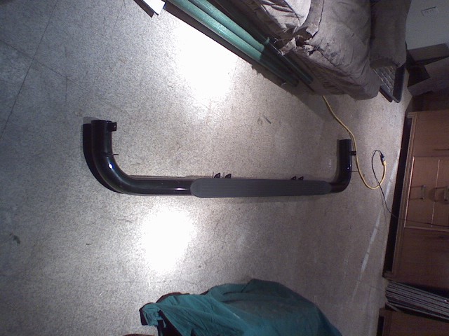 Black side step with gray tread pad, lying on a concrete floor