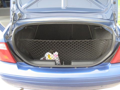 1986 Ford Bronco - The trunk of a blue car is open, revealing a cargo net and some stored items.