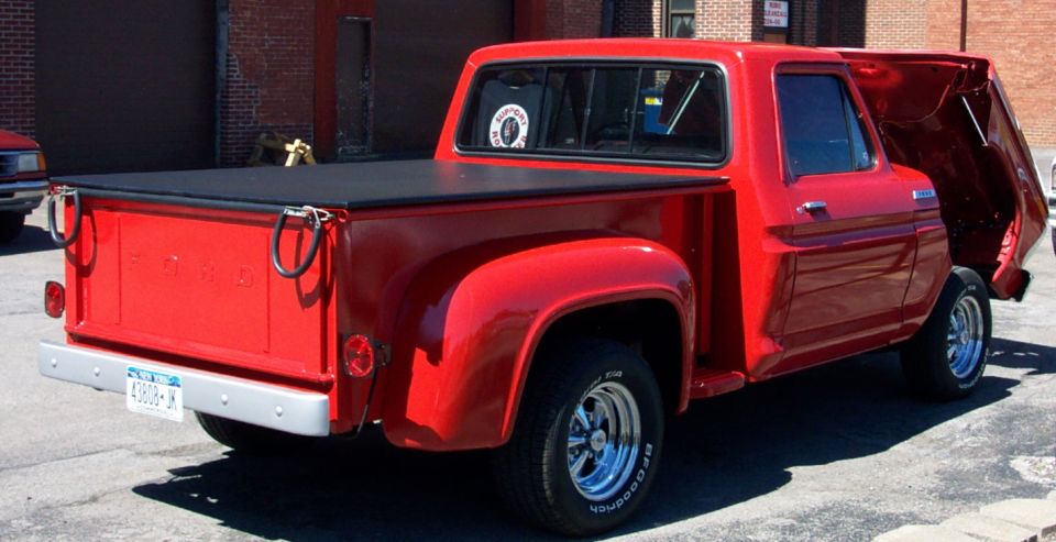 Red pickup truck with a black tonneau cover and chrome wheels, rear 3/4 view