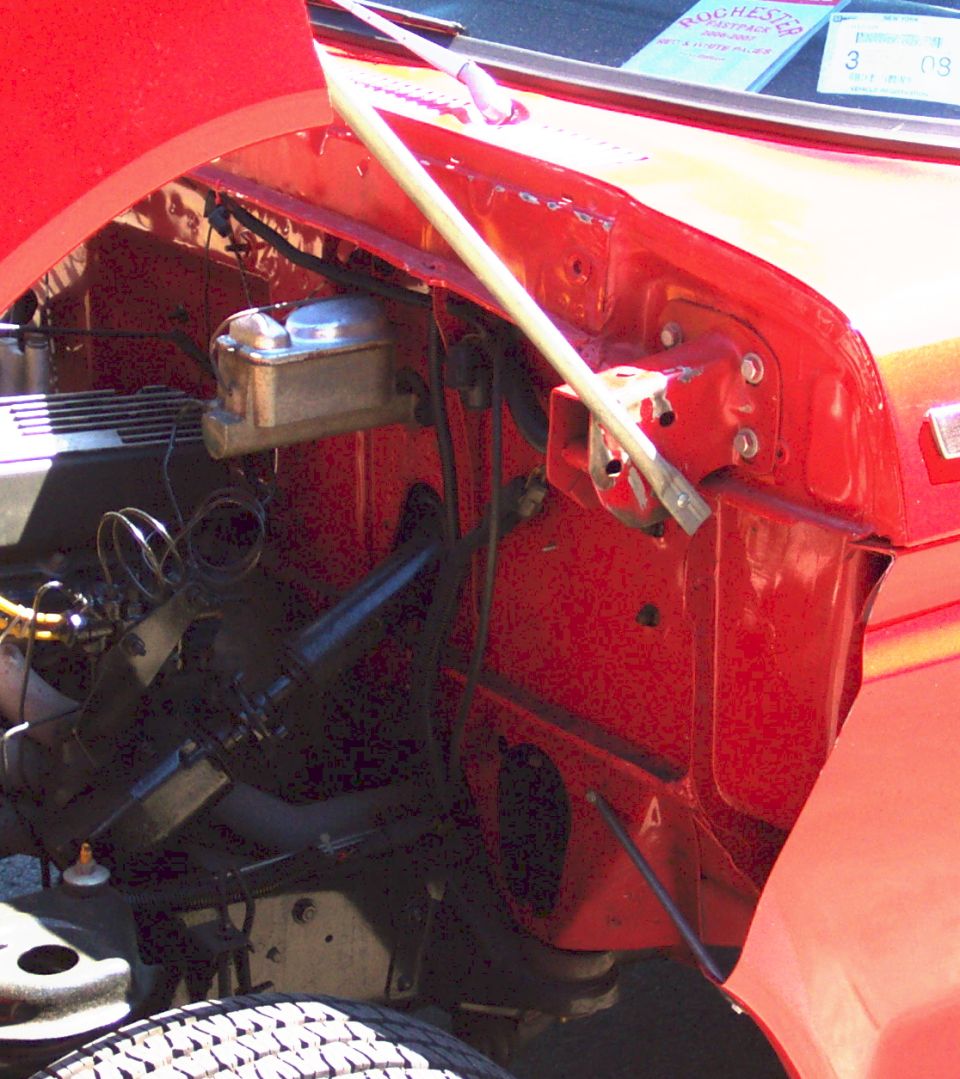 Close-up of a red car's engine bay, showing the brake fluid reservoir and various hoses