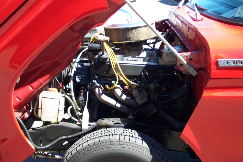 Red truck engine bay with V8 engine, air cleaner, and yellow spark plug wires. "FORD" emblem visible on fender