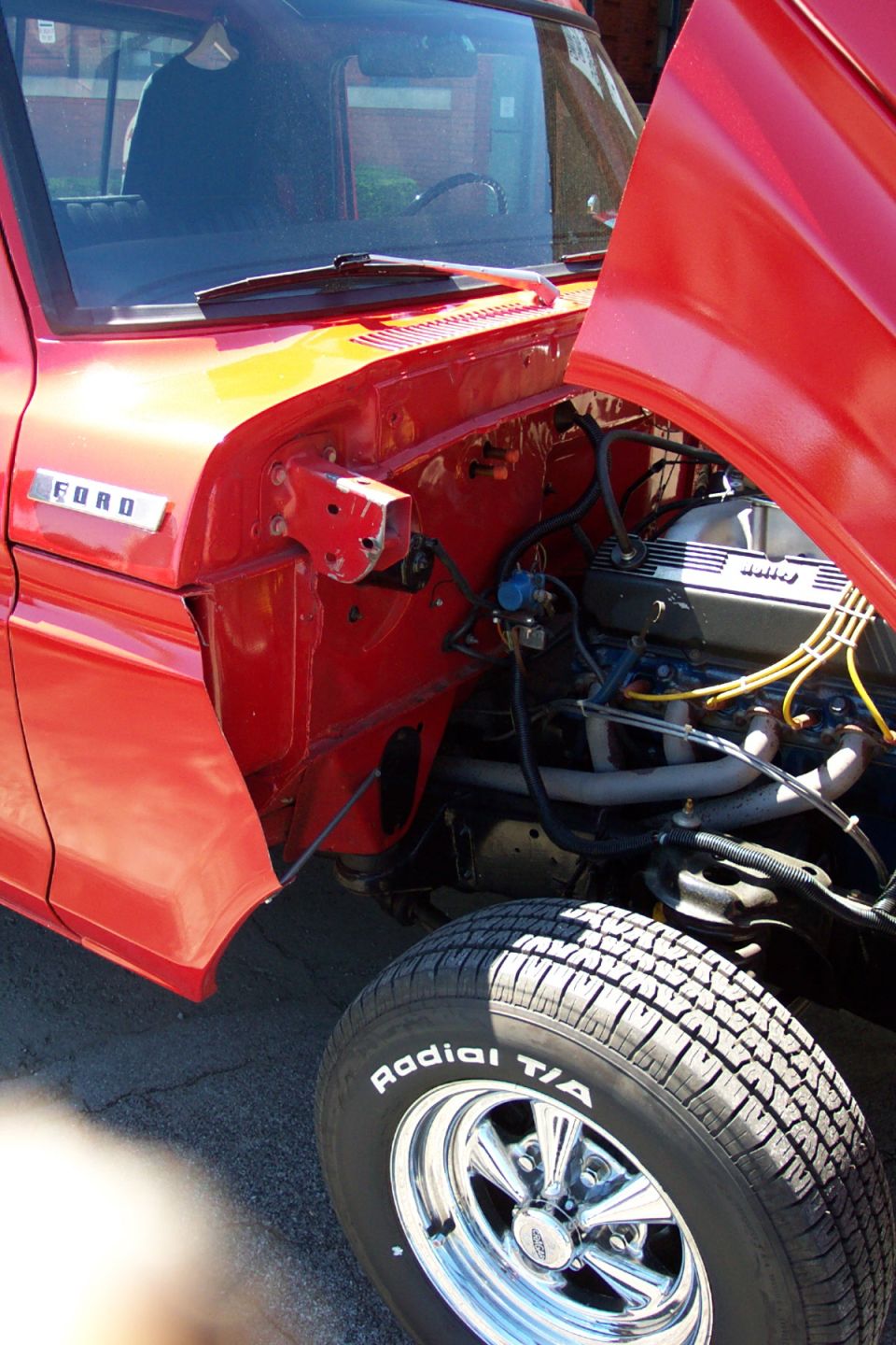 Red Ford truck engine bay with hood open, chrome wheels, and 'Radial T/A' tire