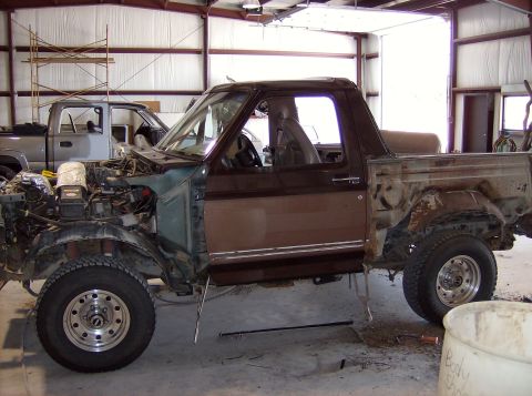 1994 Ford Bronco - This Ford Bronco is undergoing repairs in a workshop, with its engine compartment open and parts removed.