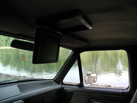 1989 Ford Bronco - The interior of a vehicle is shown, with a screen mounted overhead and a view of a river through the side window.