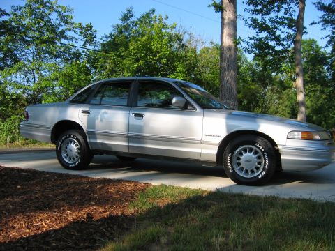 1985 Ford LTD Crown Victoria - Side profile of a silver sedan, likely a 1995 Ford Crown Victoria, parked outdoors on a sunny day.