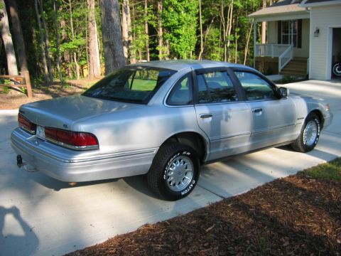 1985 Ford LTD Crown Victoria - A silver sedan is parked on a concrete driveway next to a mulched area and a house.