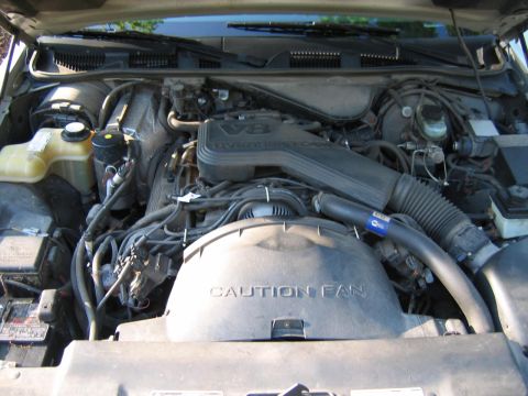 1985 Ford LTD Crown Victoria - The engine bay of a car, likely from the early 1990s, shows a V8 engine and a "CAUTION FAN" shroud.