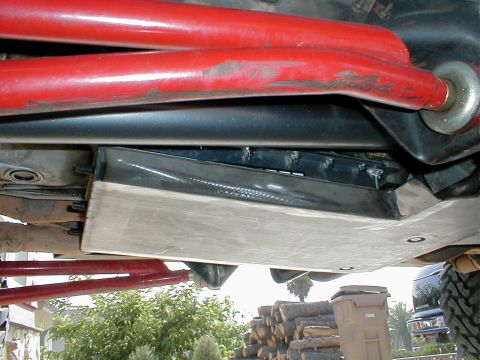 1996 Ford Bronco - The underside of a vehicle shows a skid plate and red suspension components, with a trash can and stacked wood visible.