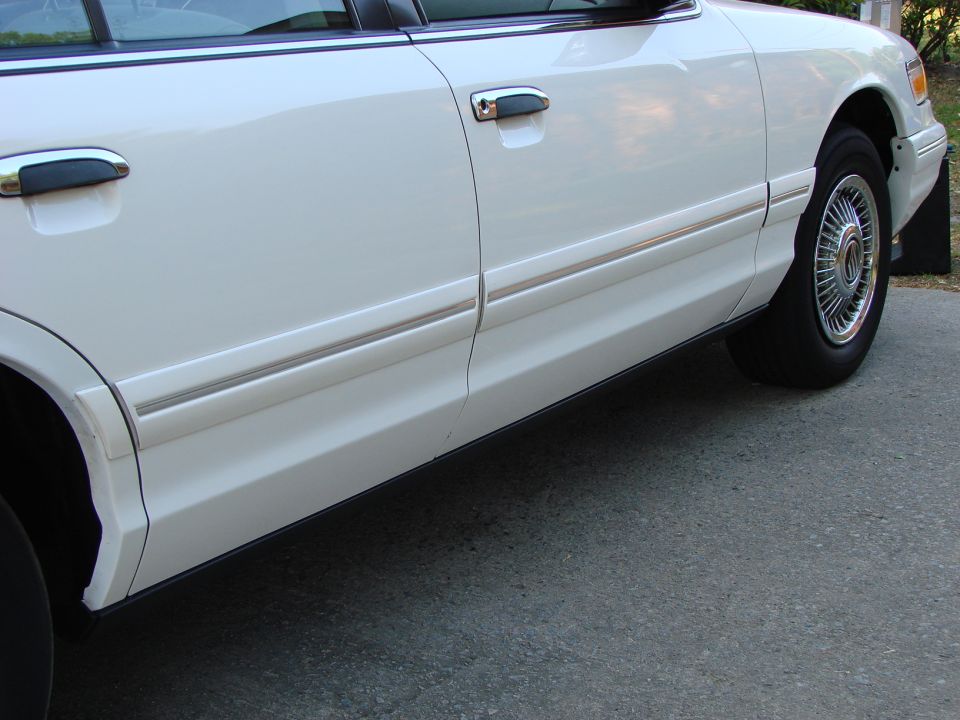 Side body detail of a white sedan showing door handles and wire wheel