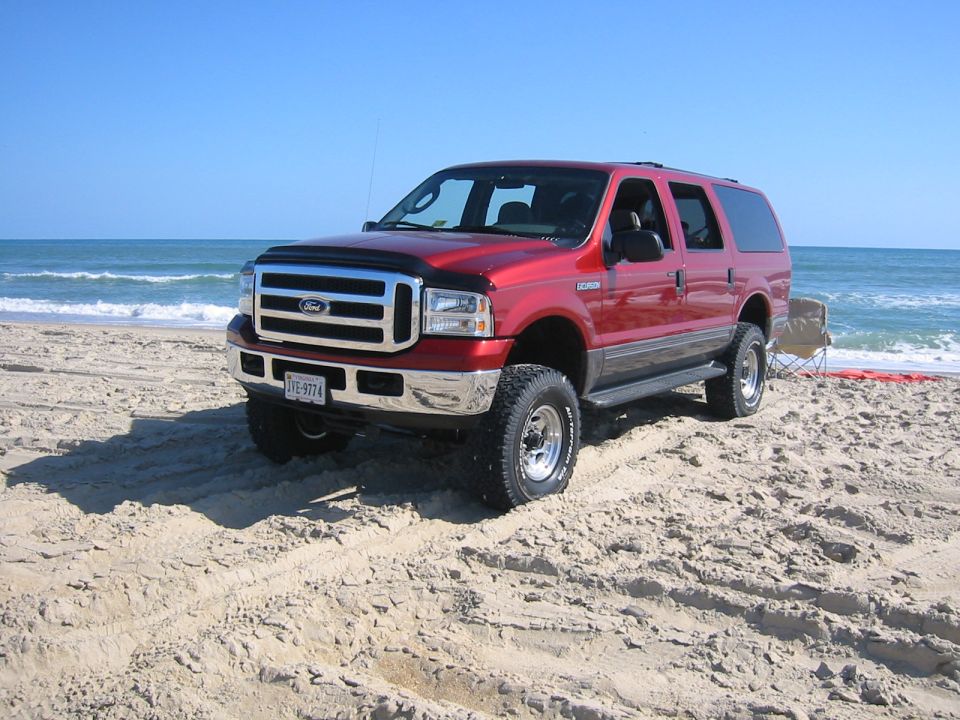 Red 2005 Ford Excursion parked on a beach with ocean in background