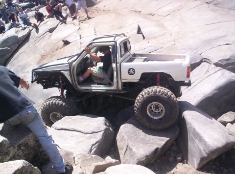 1989 Ford Bronco - Elevated side view of a white doorless mini-truck rock buggy crawling over granite slabs, running an exo-cage, tube front bumper, red coilo…