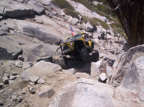 1989 Ford Bronco - Yellow topless Jeep Wrangler descending a granite boulder ledge on a rocky trail, wearing a tube front bumper with light bar, roll cage, co…