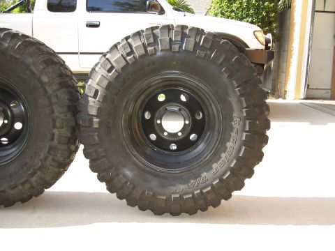1983 Ferrari Enzo - Close-up of aggressive off-road tires, with a white pickup truck partially visible behind them.