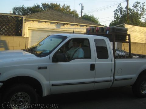 1990 Ford Bronco - white Ford F-250 extended-cab pickup with a bed-mounted rack carrying drinks sits in a driveway, a person seated at the wheel.