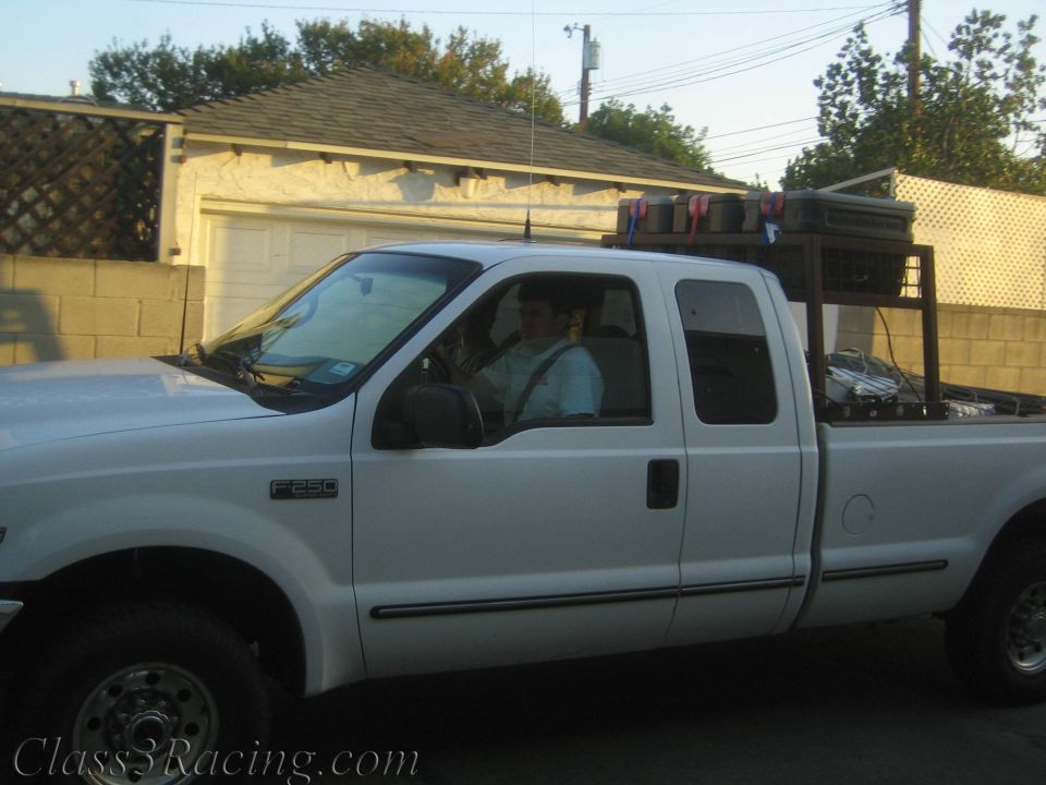 White Ford F-250 extended-cab pickup with man in driver seat parked by garage